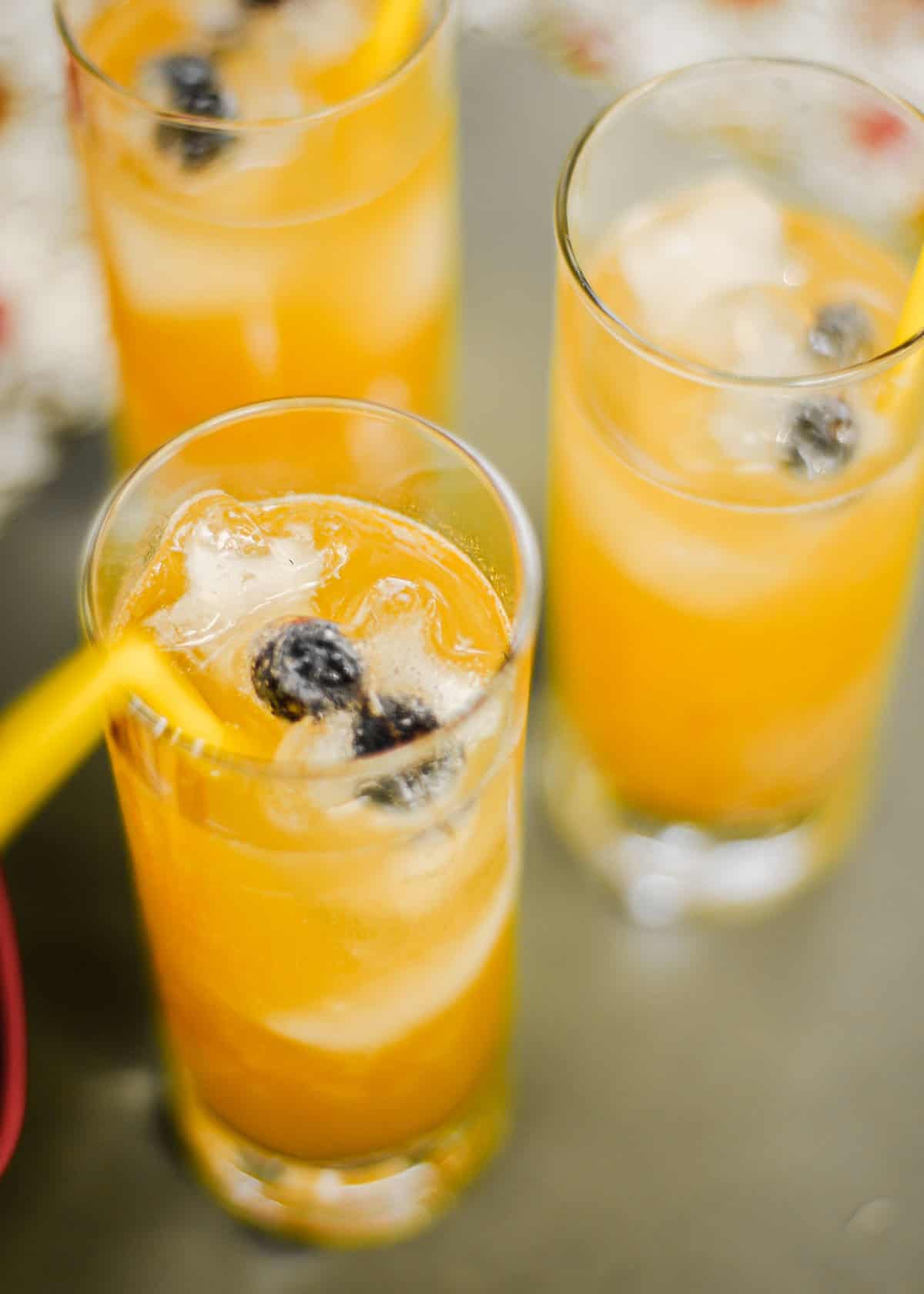 Close up of orange drink in glass with star-shaped ice cubes and blueberries.