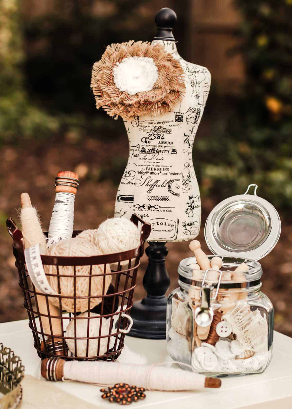 shabby chic table decorations including yarn balls and vintage spools, vintage clothes pins in jar, and mini dress form.