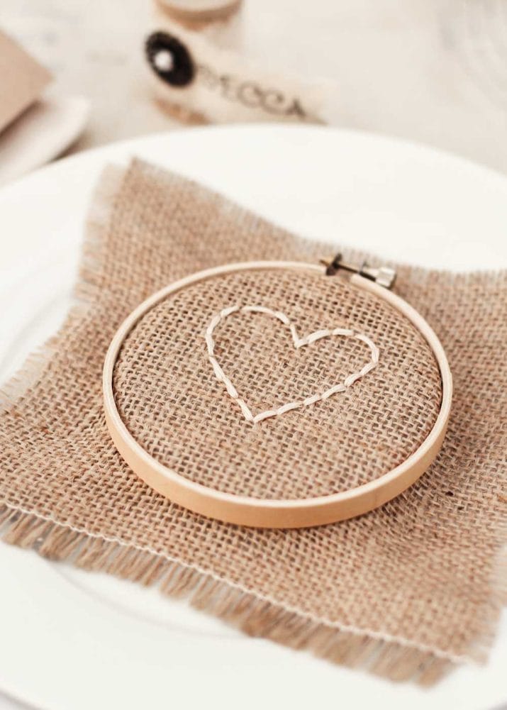 white plate with burlap square with heart shape stitched on, framed inside a wood embroidery hoop. 