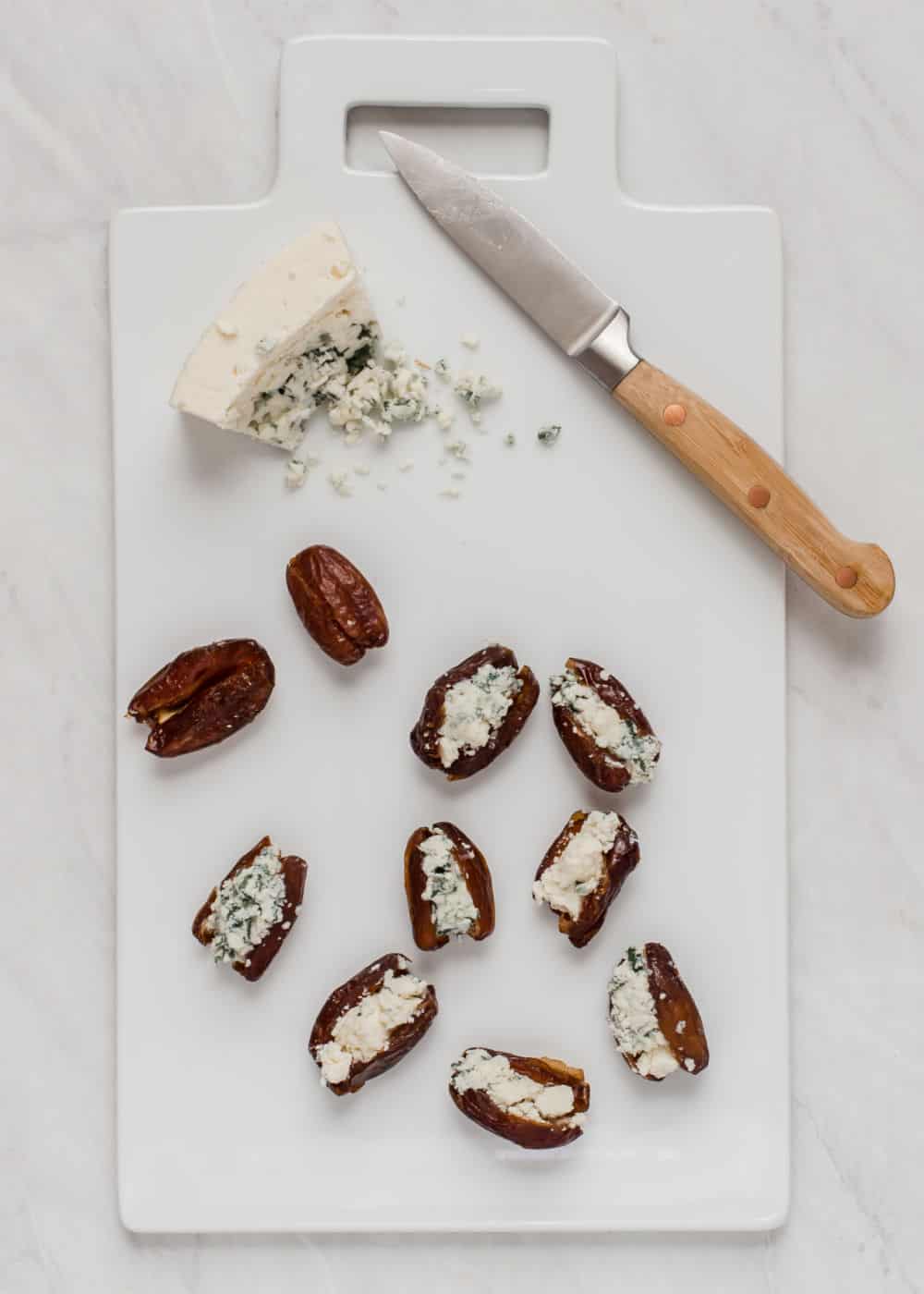 dates cut in half, filled with blue cheese, on white cutting board with knife.