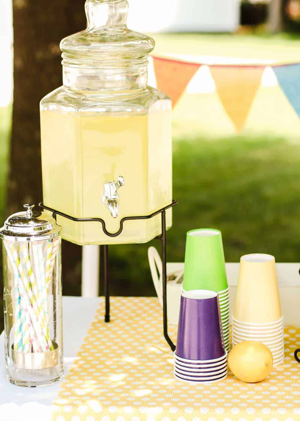 outdoor table with drink dispenser and colorful paper cups and straws.