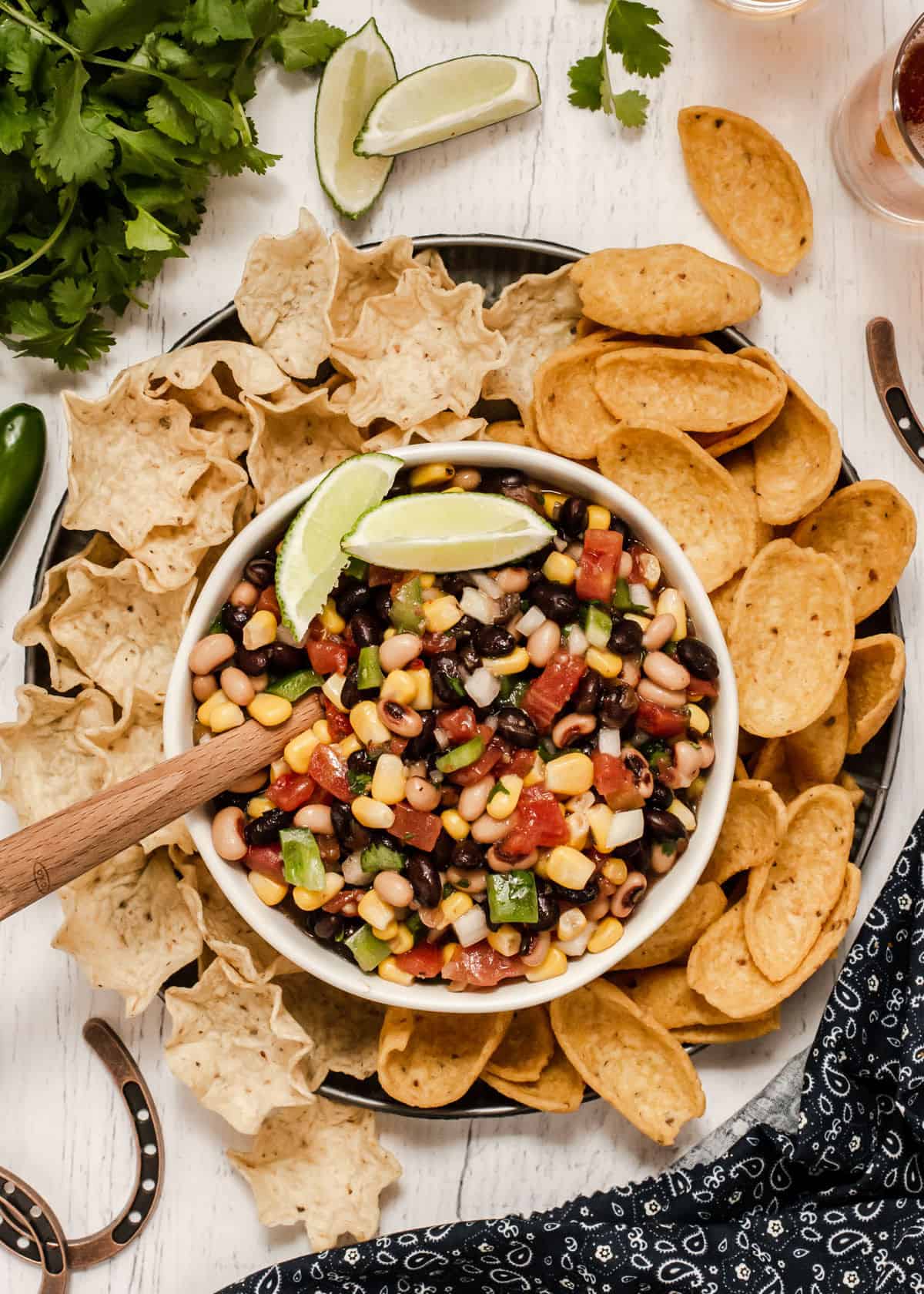 overhead view of bowl filled with black bean, pinto beans, corn and tomato dip surrounded by tortilla scoops and Fritos scoops.