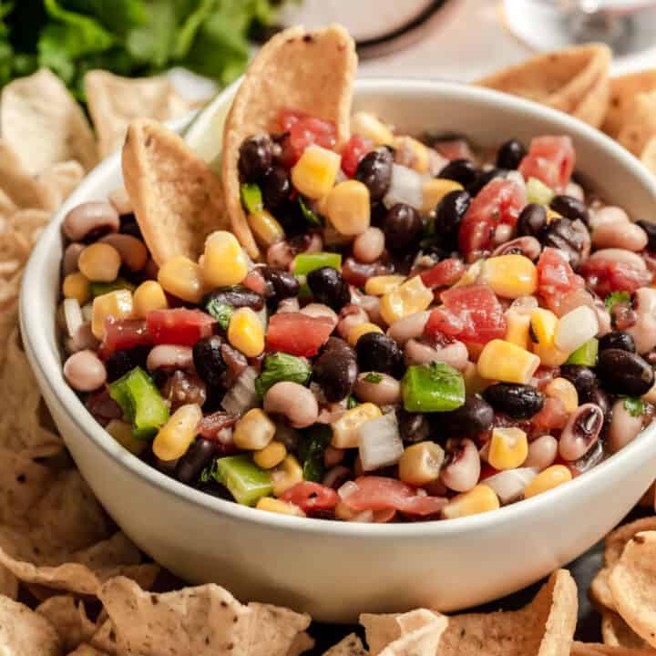 bowl filled with black bean, pinto beans, corn and tomato dip surrounded by tortilla scoops and Fritos scoops.