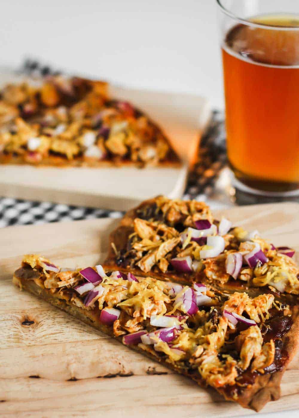 Slices of thin crust barbecue chicken pizza with cheddar and purple onions, on wood board with glass of beer.