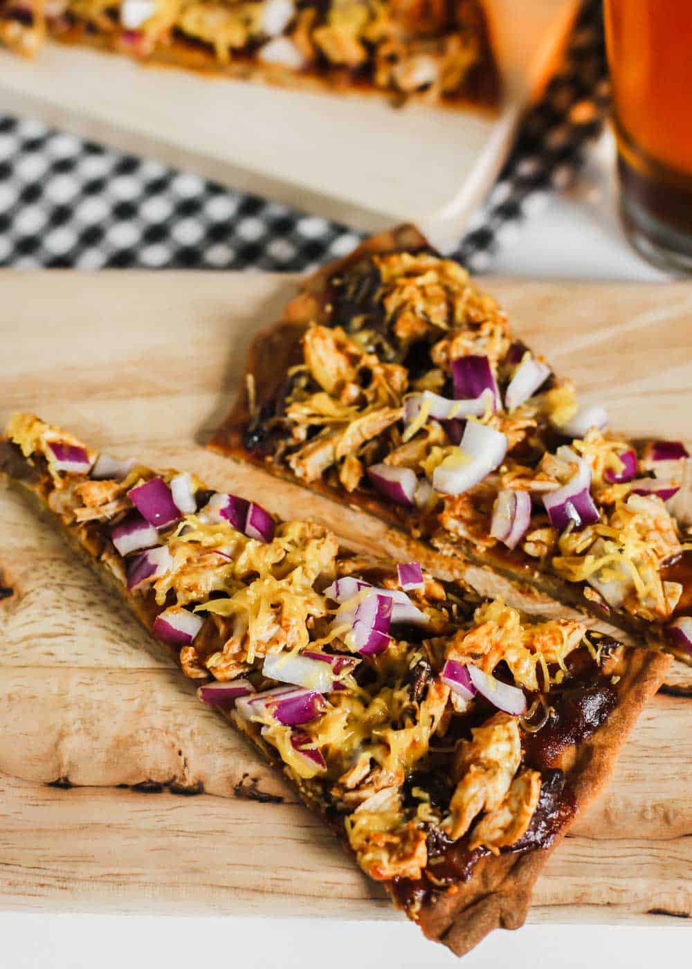 two slices of thin crust barbecue chicken pizza with cheddar and purple onions.