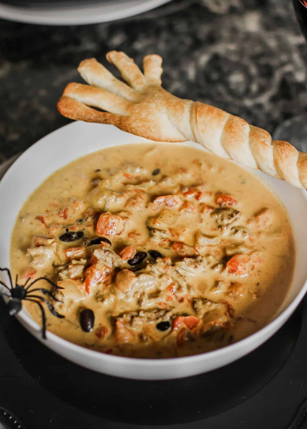 Halloween theme chili in white bowl with broom shaped breadstick and spider decoration.