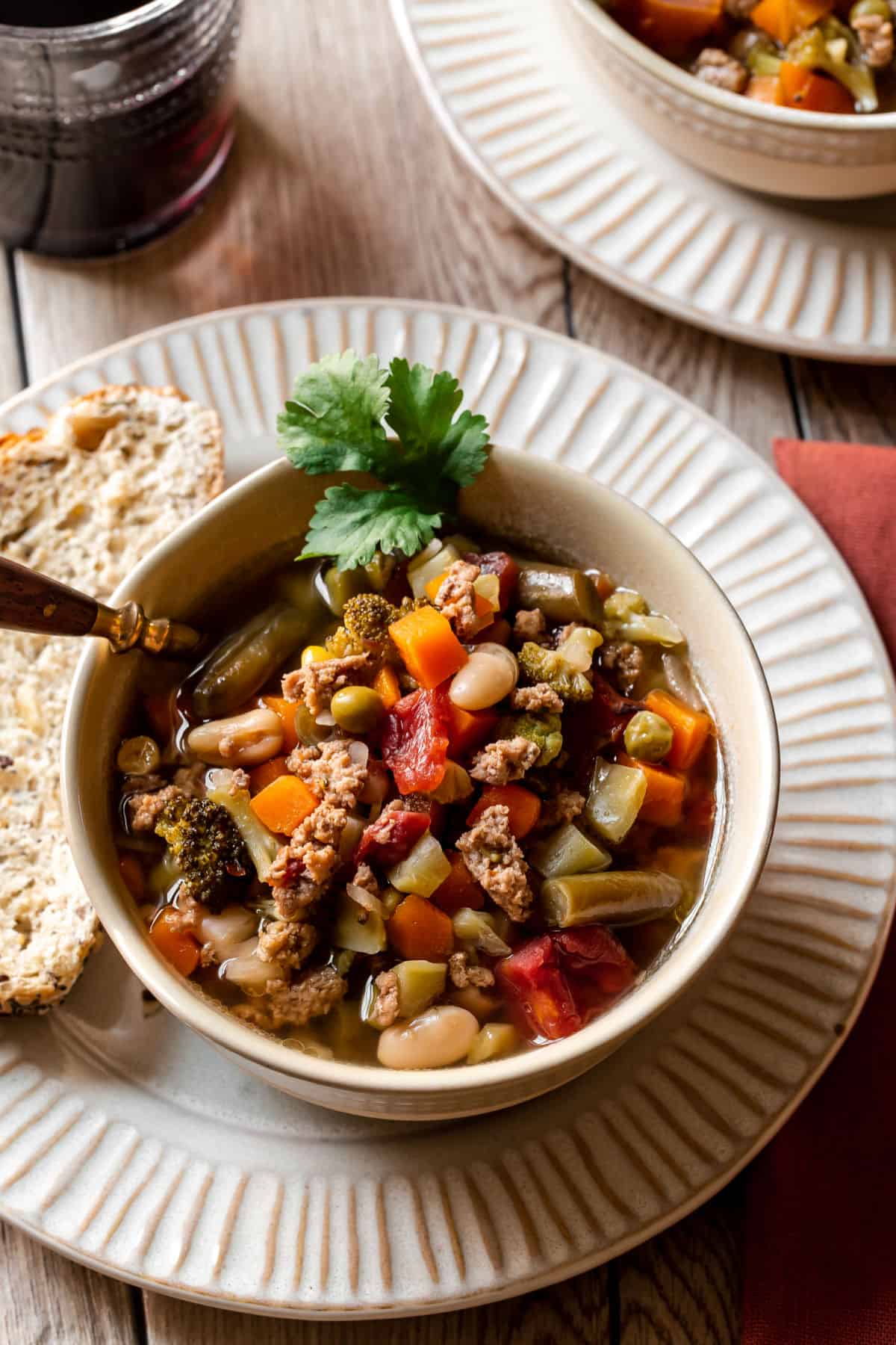 ground turkey with vegetables soup in bowl on cream plate with bread slice, overhead