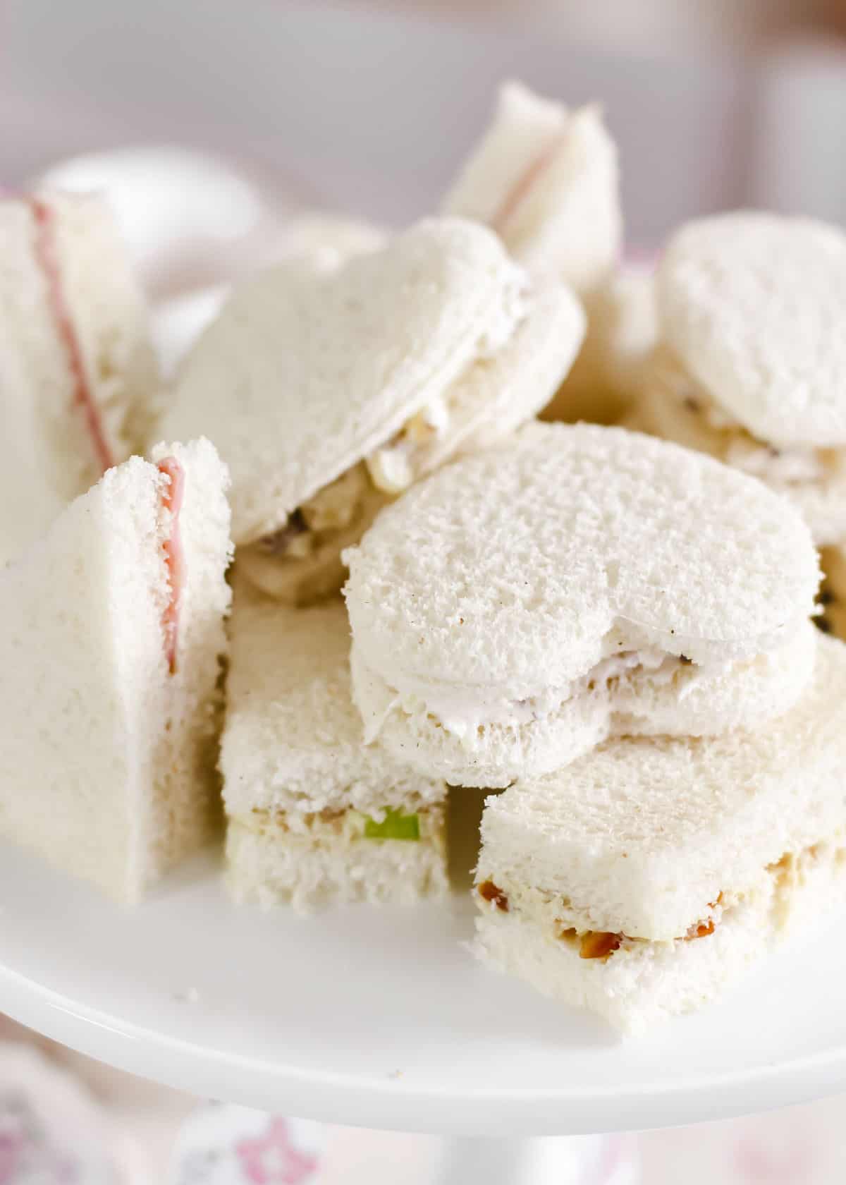 tea party finger sandwiches cut into different shapes, piled on white dish.