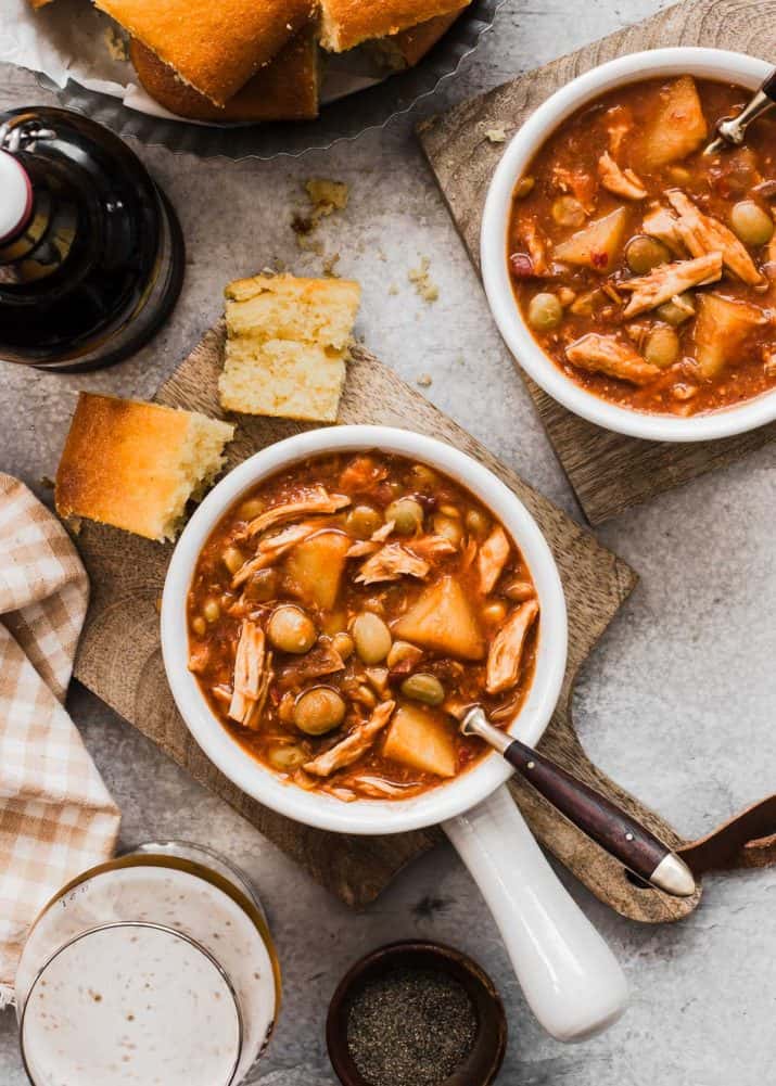 two white bowls of Brunswick stew with cornbread and drinks on table.