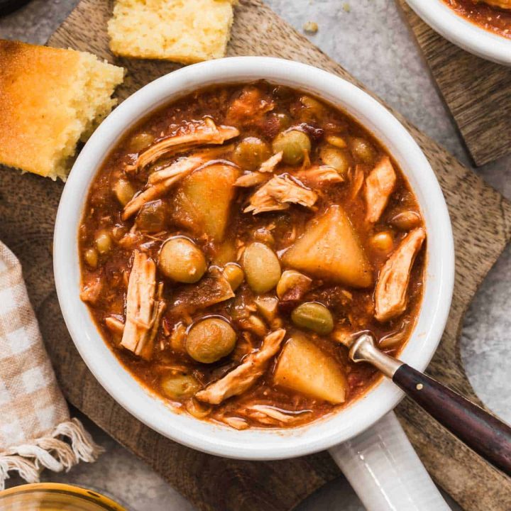 Brunswick stew in white bowl with handle, and spoon inside.