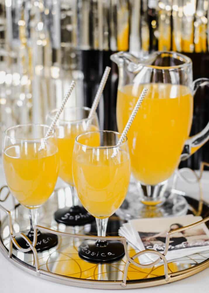 three glasses and a pitcher filled with golden colored punch, on tray.