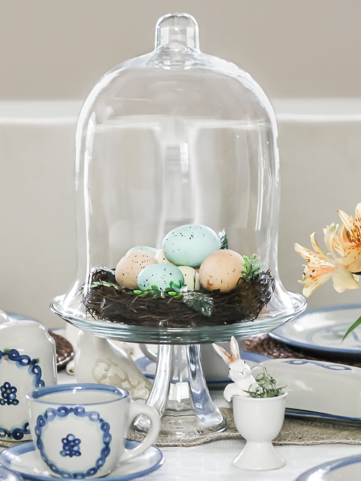 Easter centerpiece with birds nest filled with eggs under glass cloche.