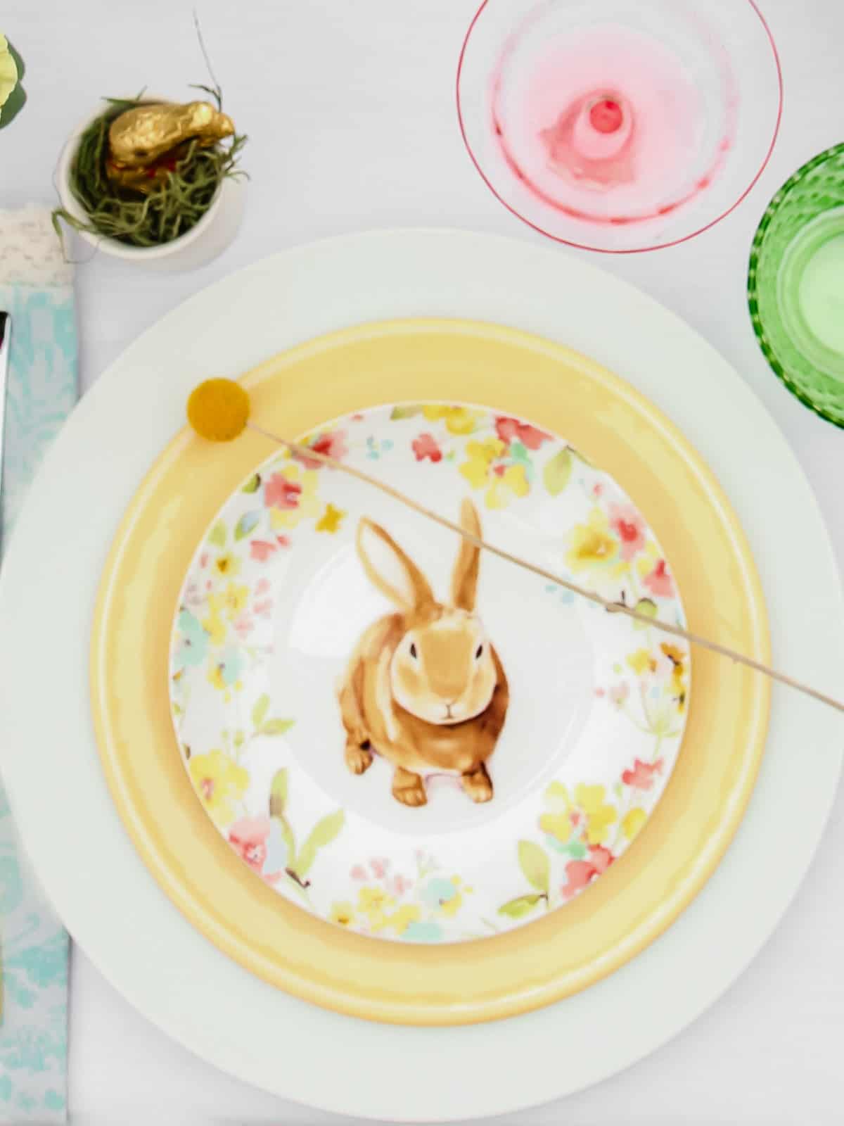 Easter themed salad plate layered on top of yellow plate and white dinner plate, on white tablecloth.