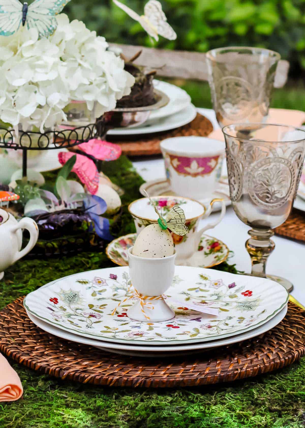 Easter table outside with vintage dishes, egg cups, and moss runner.