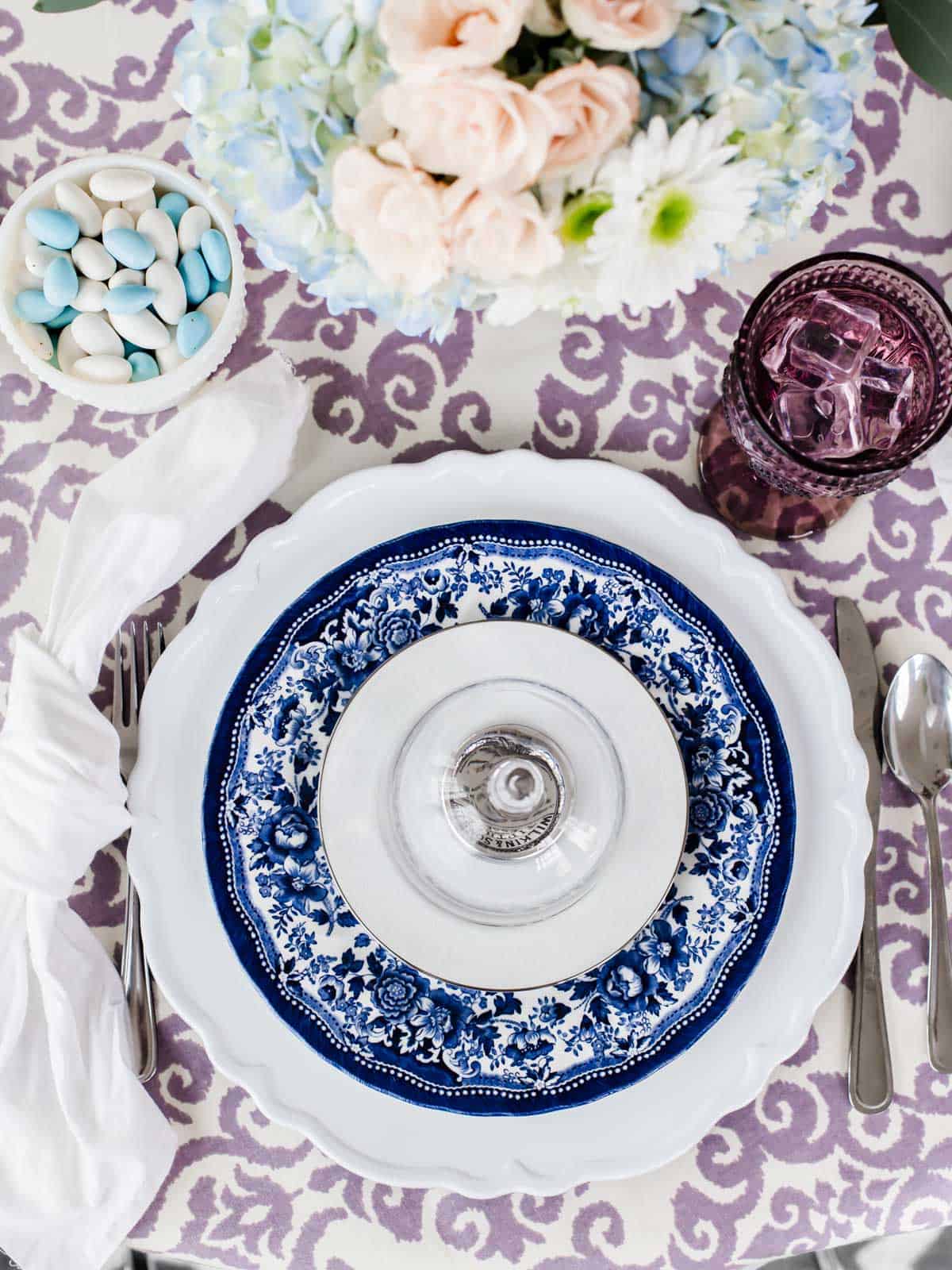 table setting with layered Blue Willow dinner plate and white salad plate on white charger, on purple print tablecloth.
