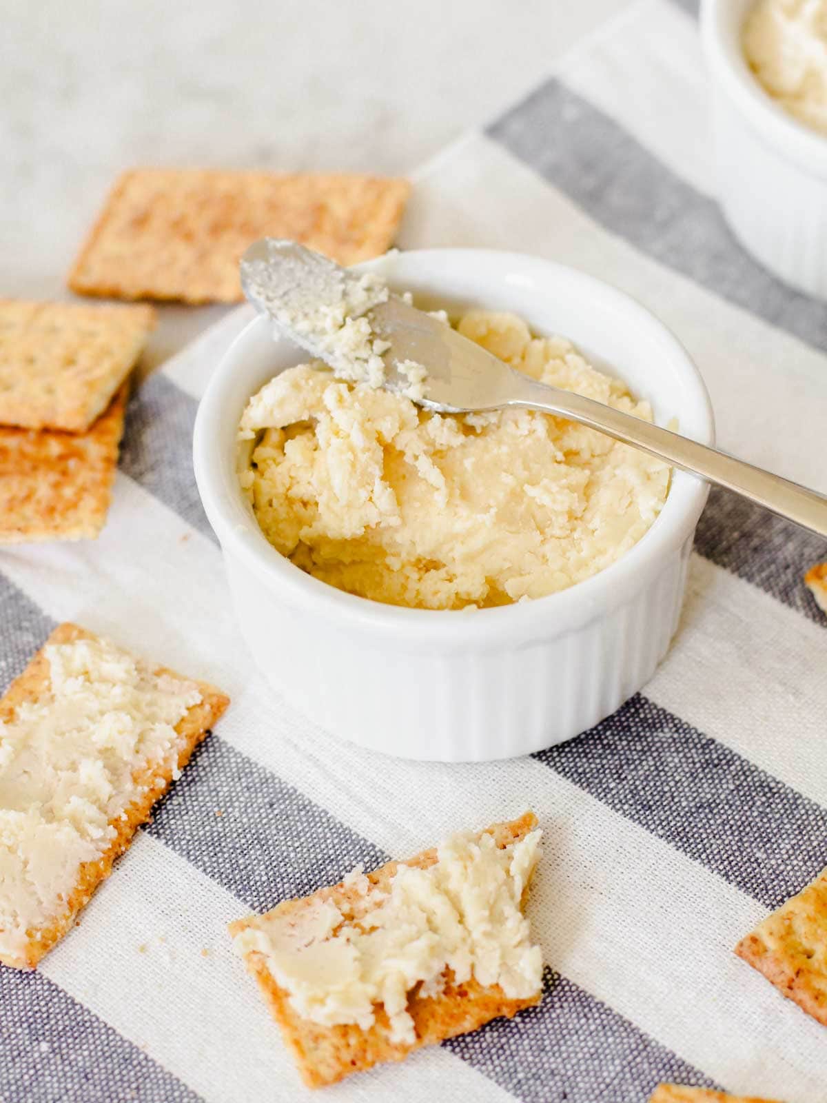 beer cheese spread in white ramekin with spreader knife on top and crackers surrounding.
