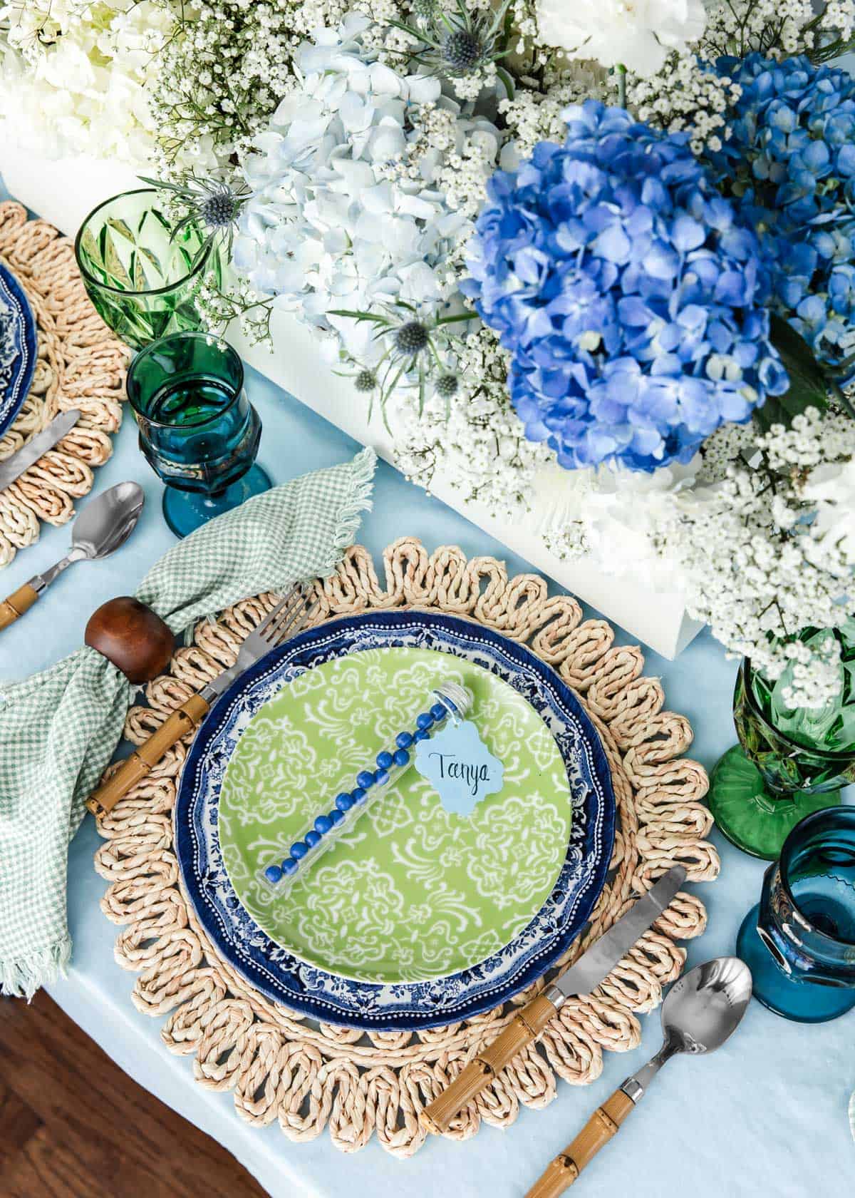 table setting with layered Blue Willow dinner plate and green salad plate on rattan place mat, with blue hydrangea centerpiece.