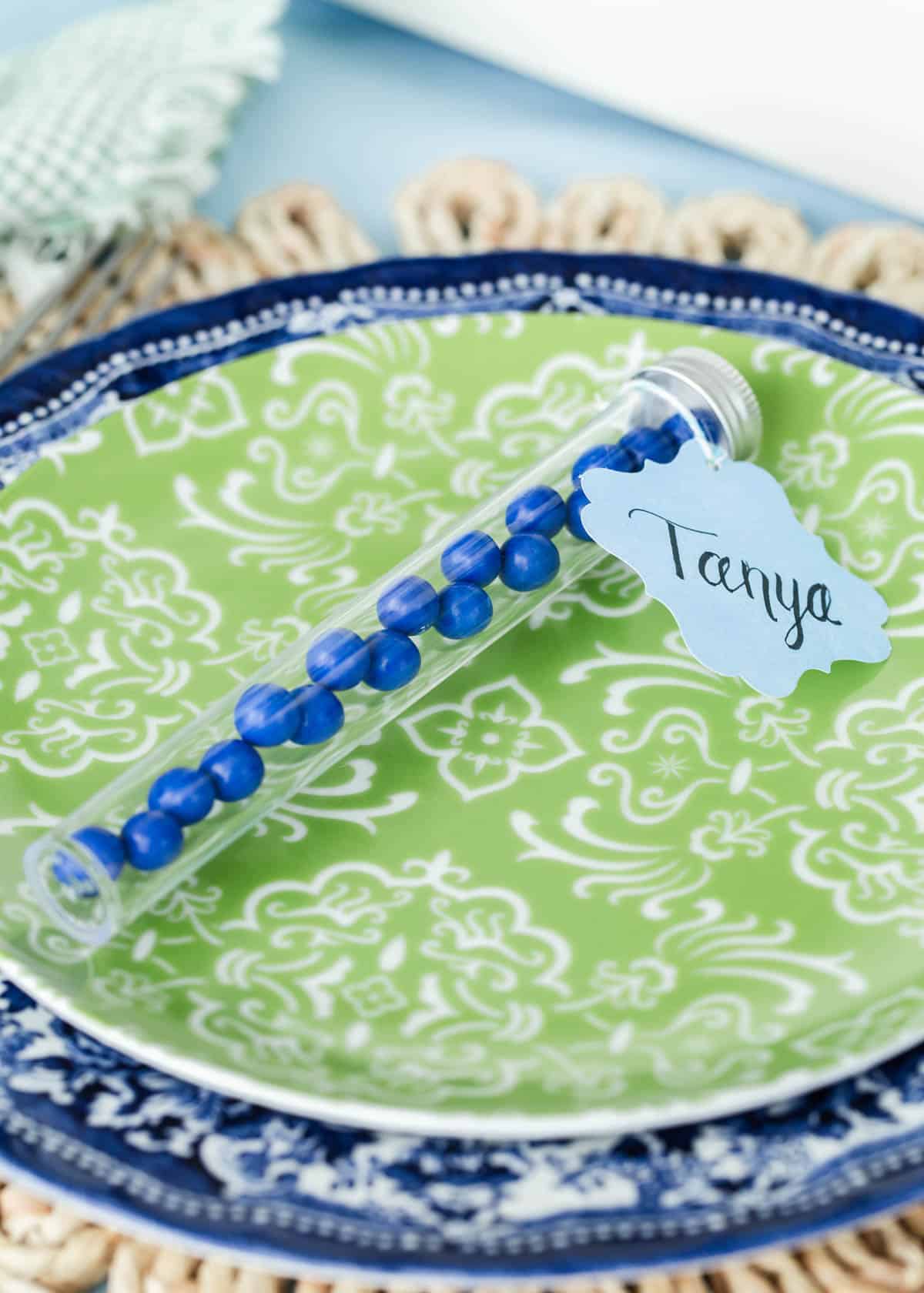 blue candies in clear tube with name tag tied on, sitting on green plate.