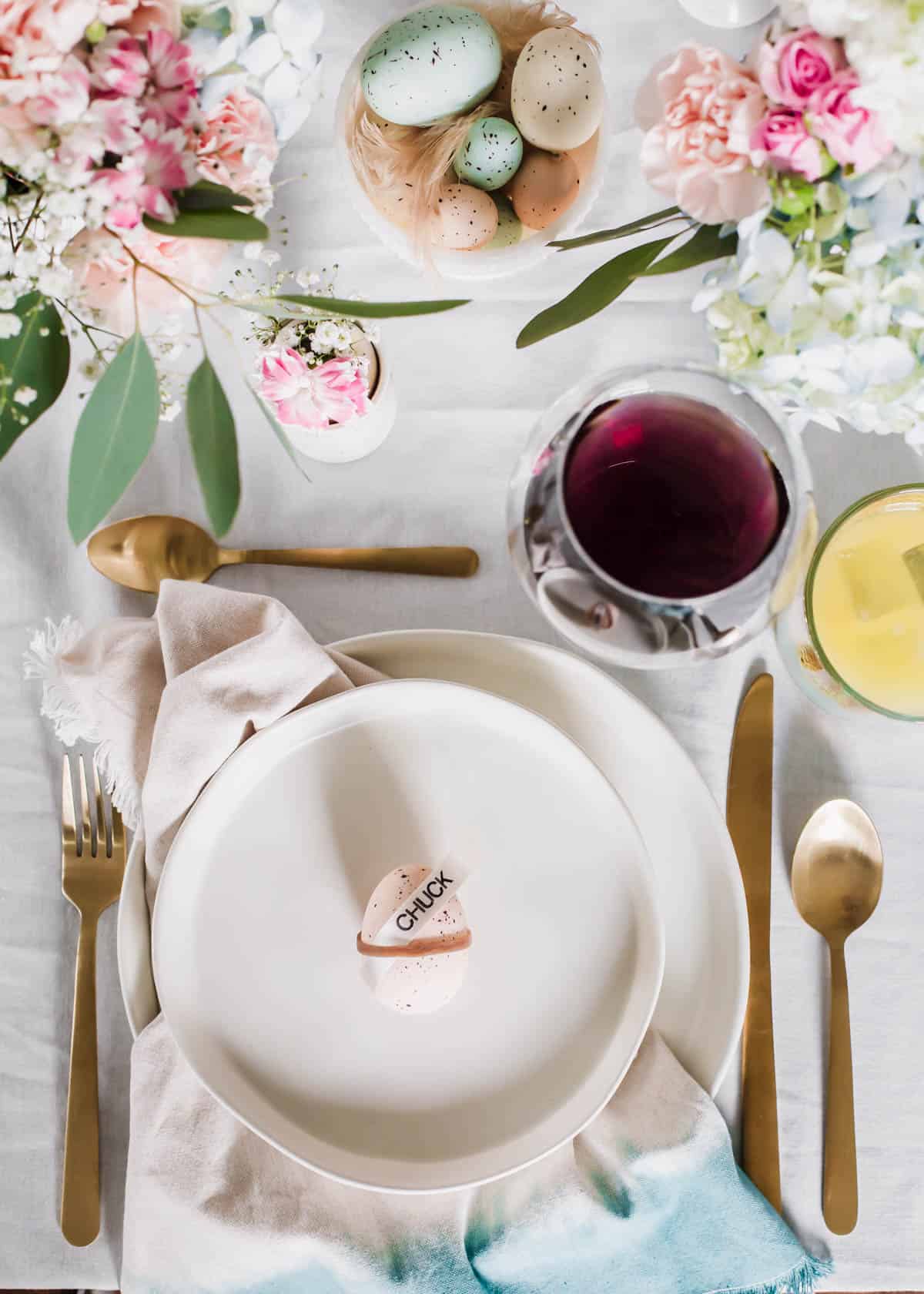 Easter place setting with egg place card holder, eggs in bowl, and flowers centerpiece.