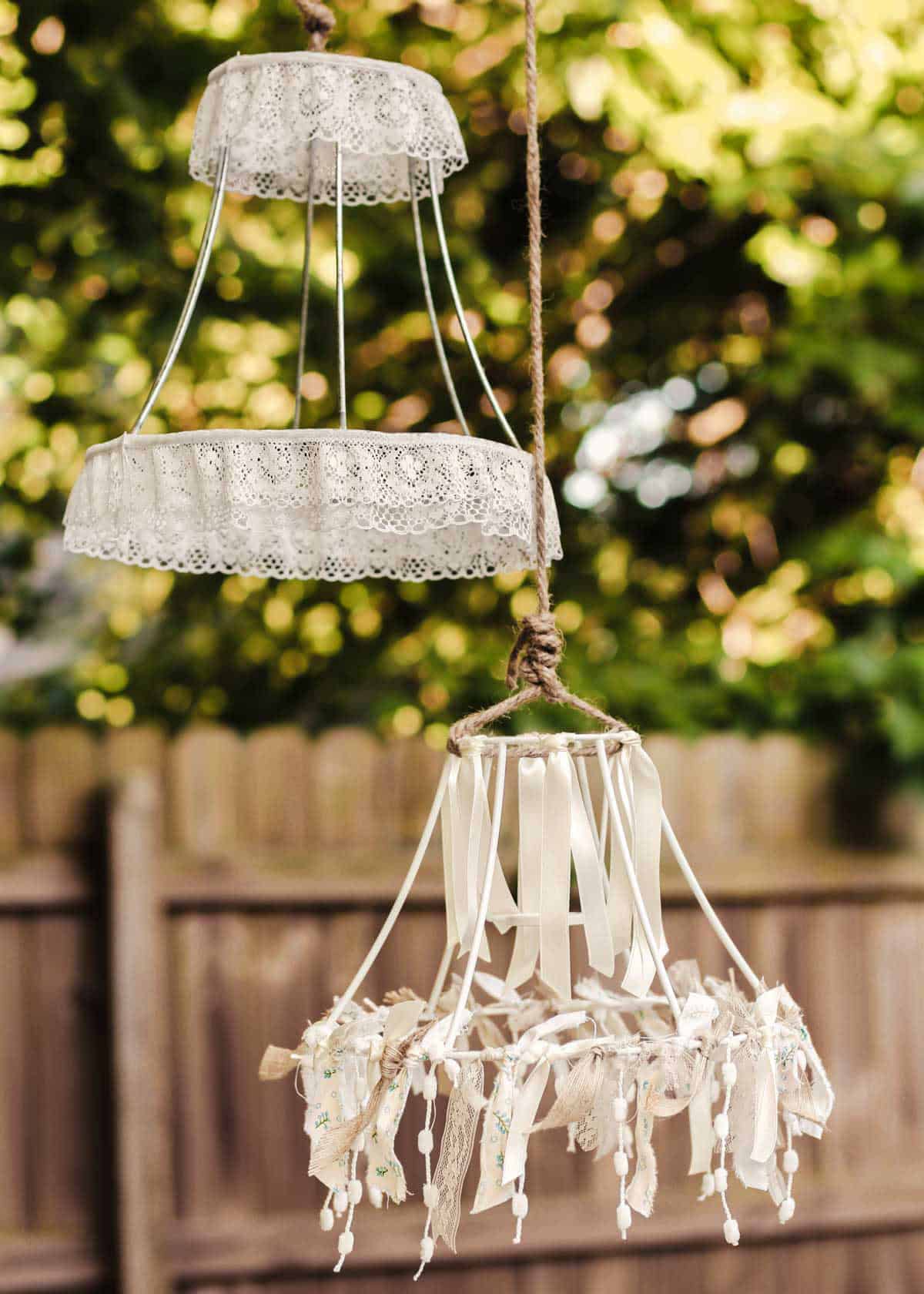 lamp shade wire frames decorated with ribbon and lace, hanging outdoors.