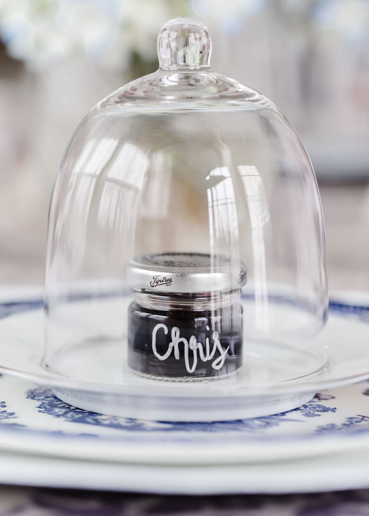 mini jelly jar with name written on it with marker, under glass cloche on dinner plate.