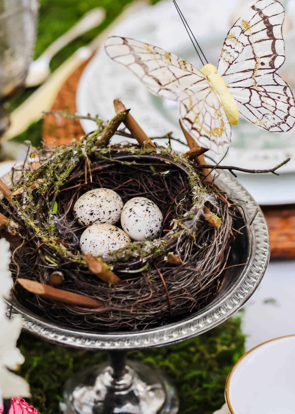 bird nest centerpiece with 3 eggs inside, sitting on silver pedestal dish.