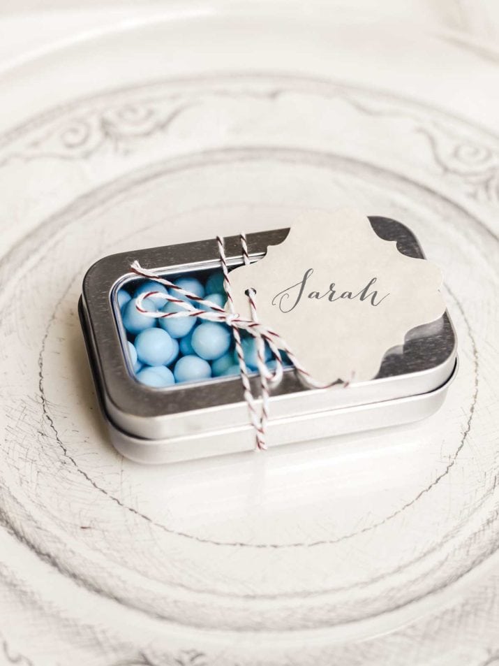 small silver tin filled with blue candies and tied with a name tag.