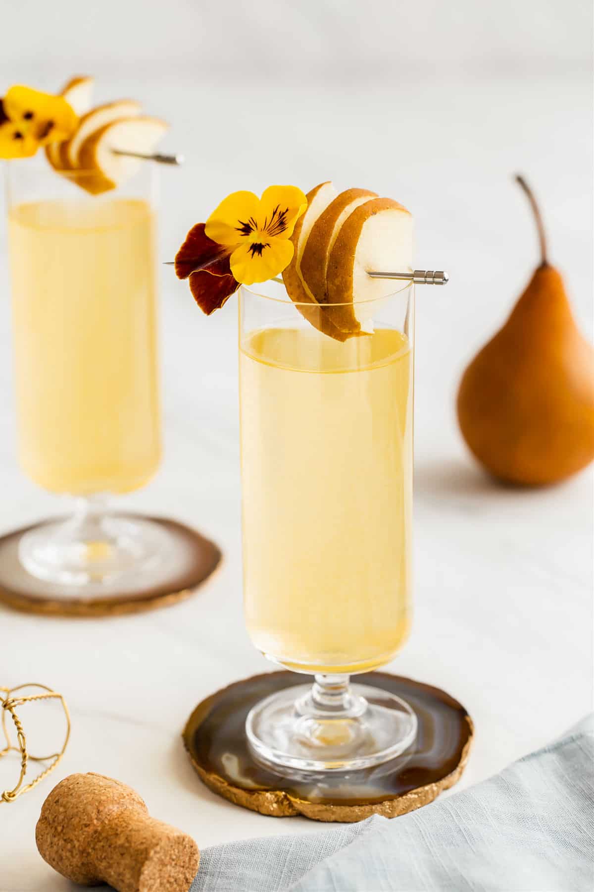two glasses with yellow drink and sliced pear garnish