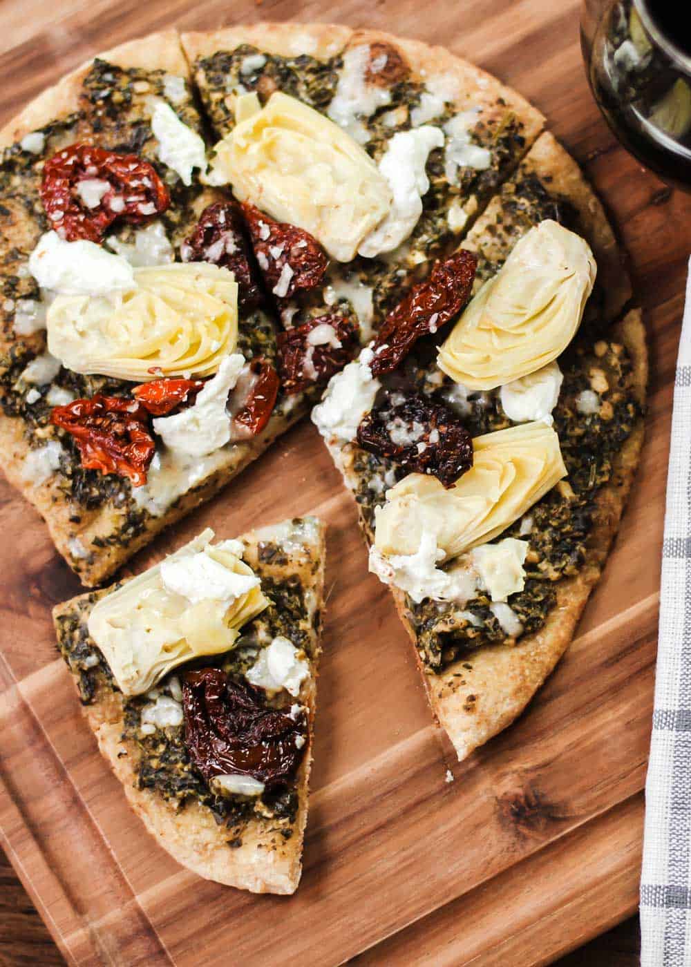 pizza on wood board, with artichokes, pesto, and sundried tomatoes.