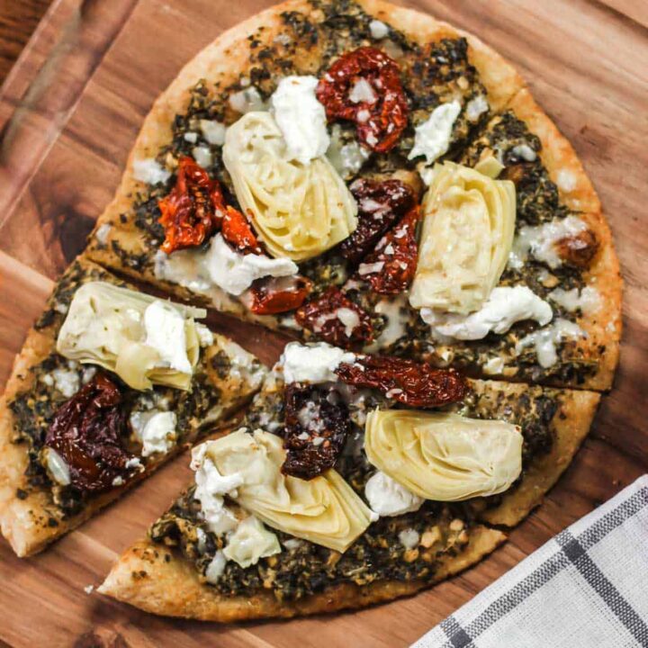 pizza on wood board, with artichokes, pesto, and sundried tomatoes.