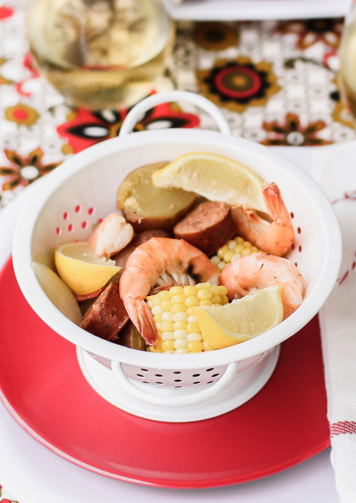 shrimp boil ingredients served in white colander on red plate.