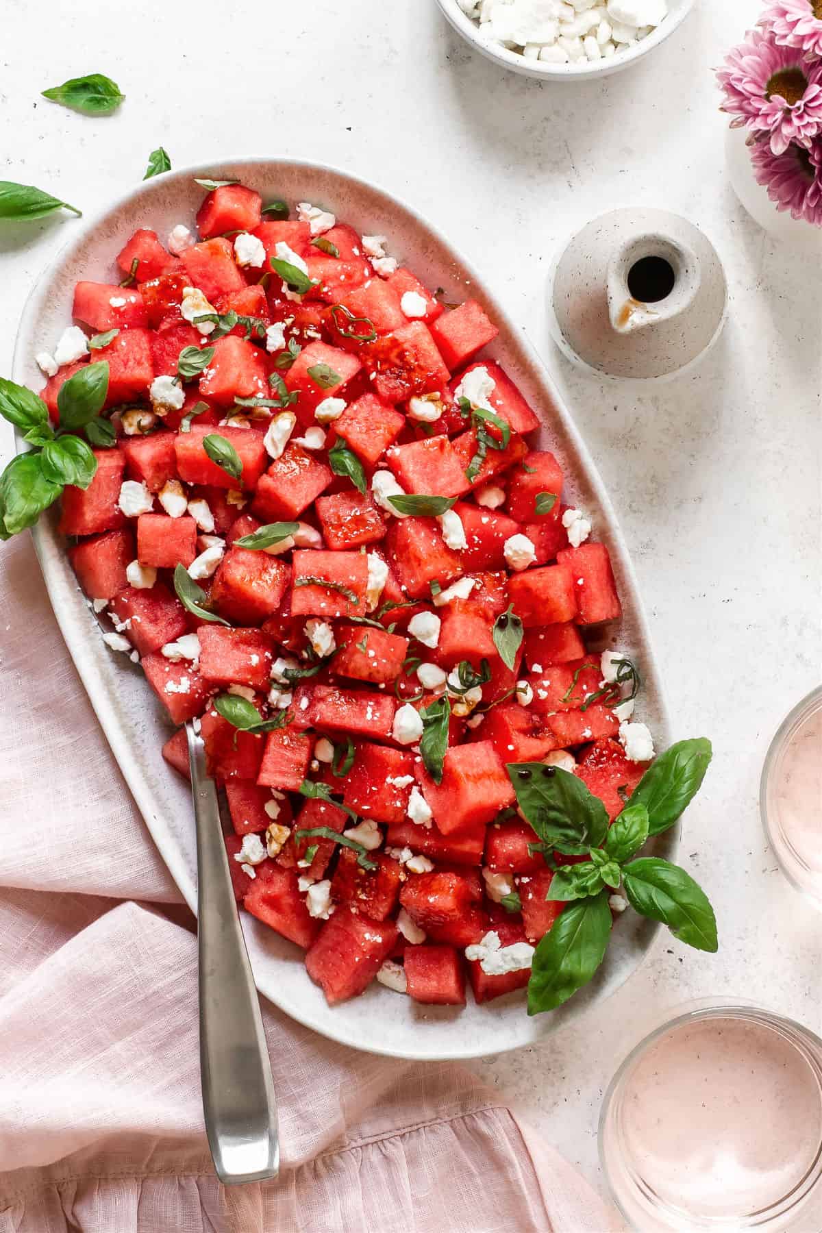 watermelon salad with basil and feta on white platter with pink napkin