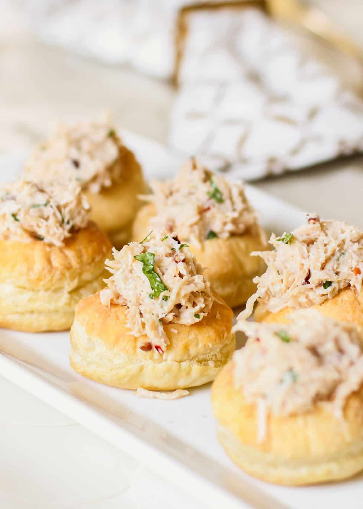 chicken salad in puff pastry cups on white serving tray.