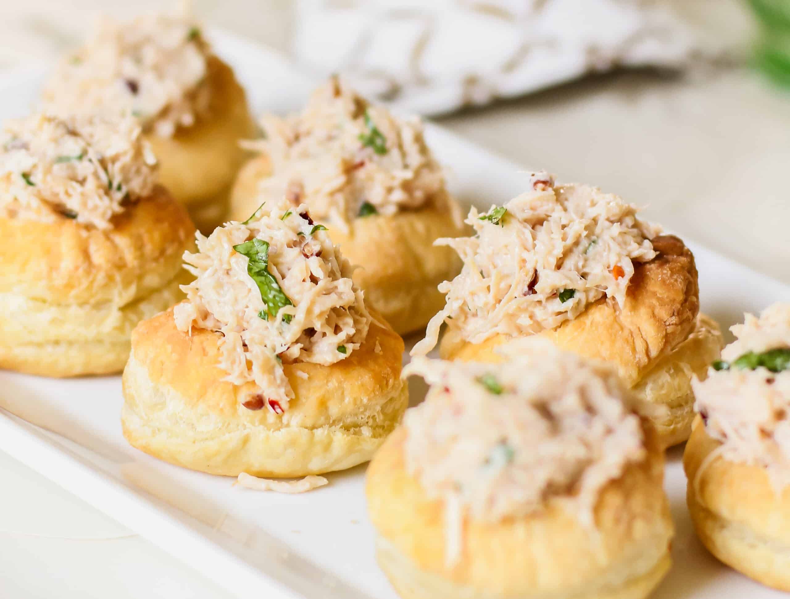 chicken salad in puff pastry cups on white serving tray.