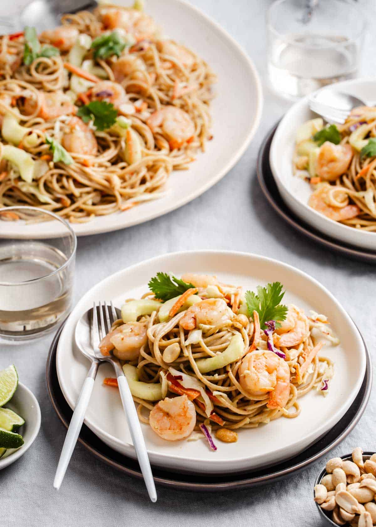 cold noodle salad with shrimp on small dinner plates, with large platter in background.