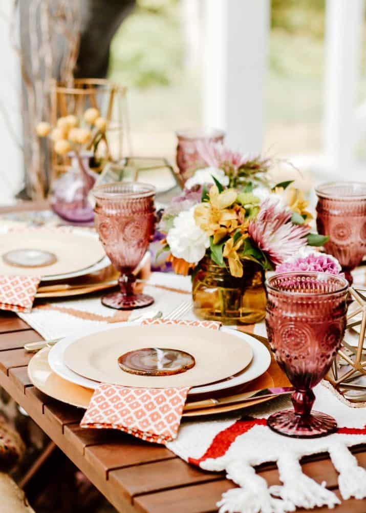 outside tablescape set up for a dinner party, with colorful glasses, flowers and neutral place settings.