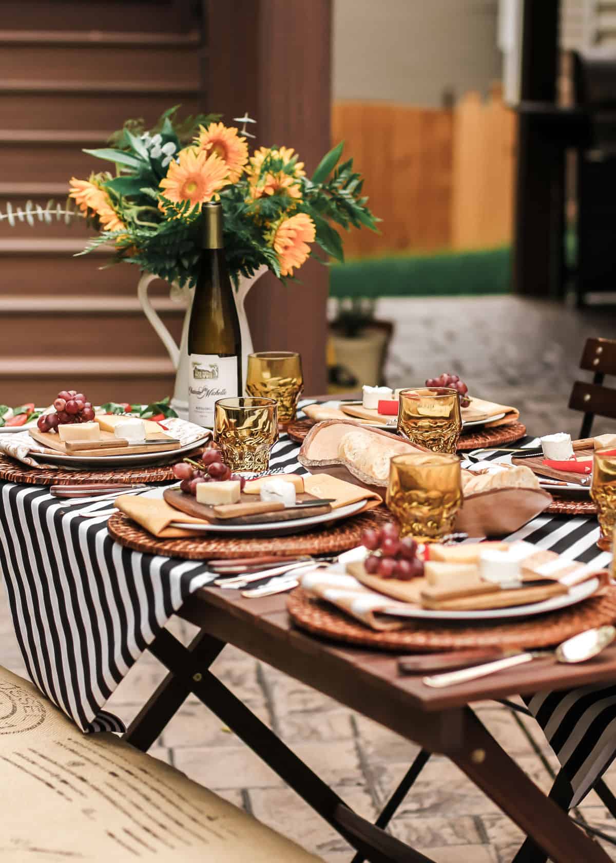 outdoor tablescape with black and white stripe table cover and yellow accents and sunflowers.