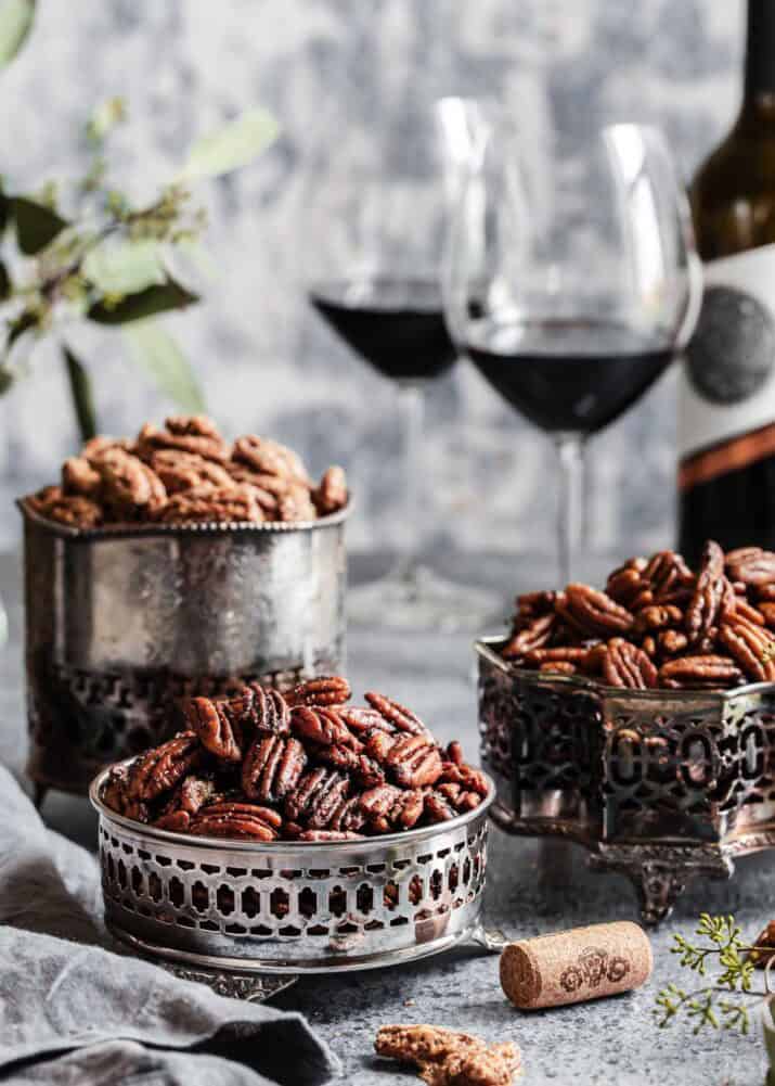 three bowls of different seasoned pecans, on table with glasses of red wine.
