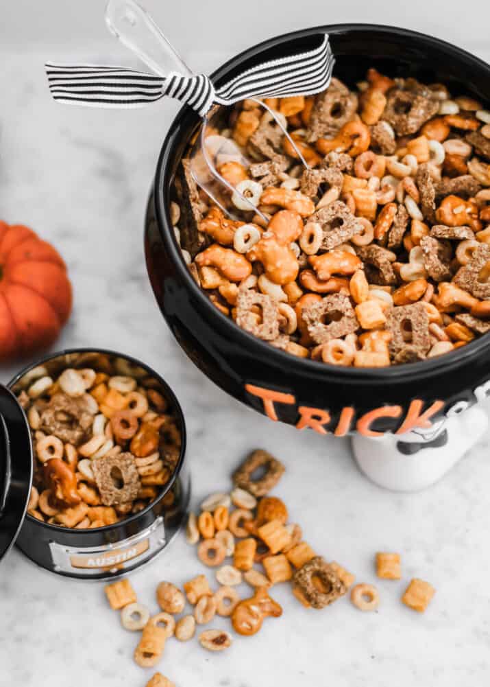 snack mix in black bowl with scoop inside, and small cup filled with mix on the side.