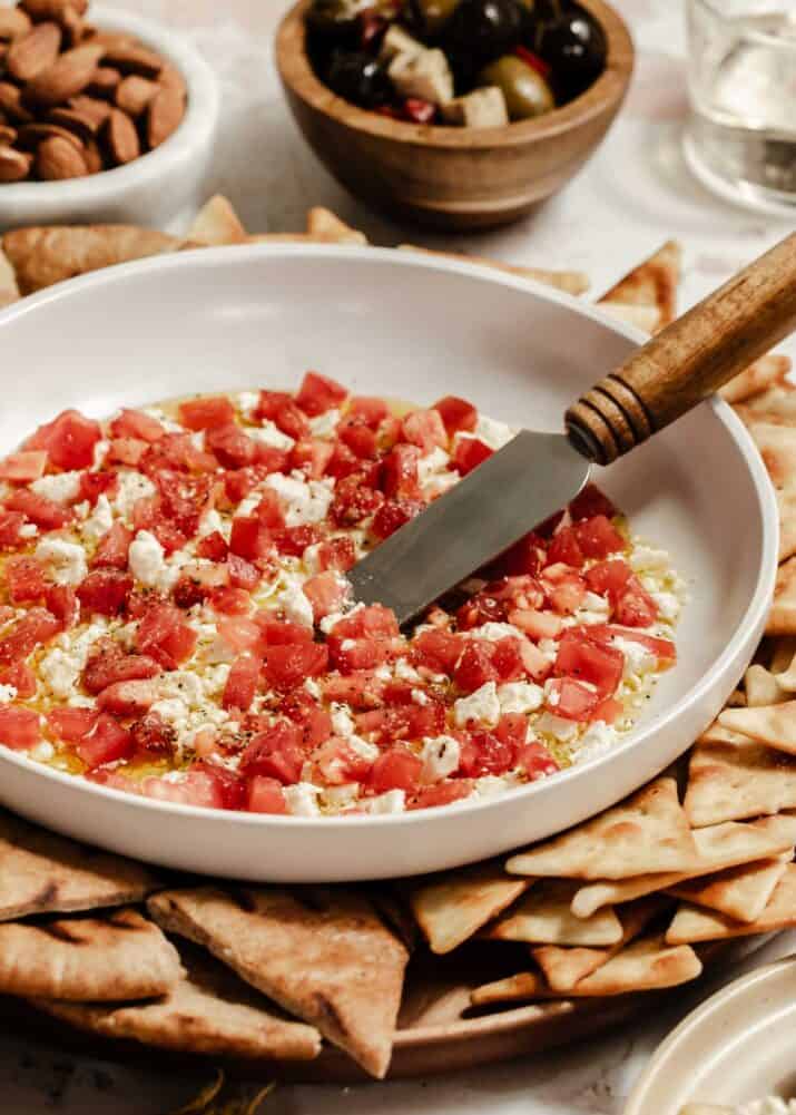 round dish with diced tomatoes, feta cheese and olive oil dip inside, surrounded by pita chips.