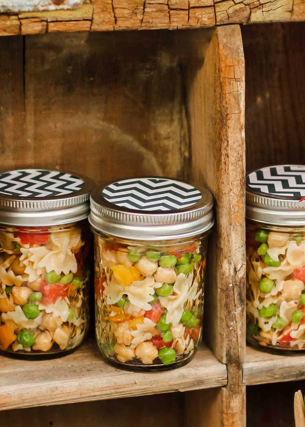 mason jars filled with pasta salad sitting in wood crate.