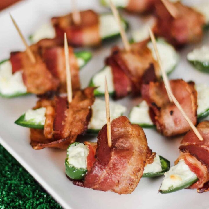 Jalapeno poppers wrapped in bacon, on white plate.