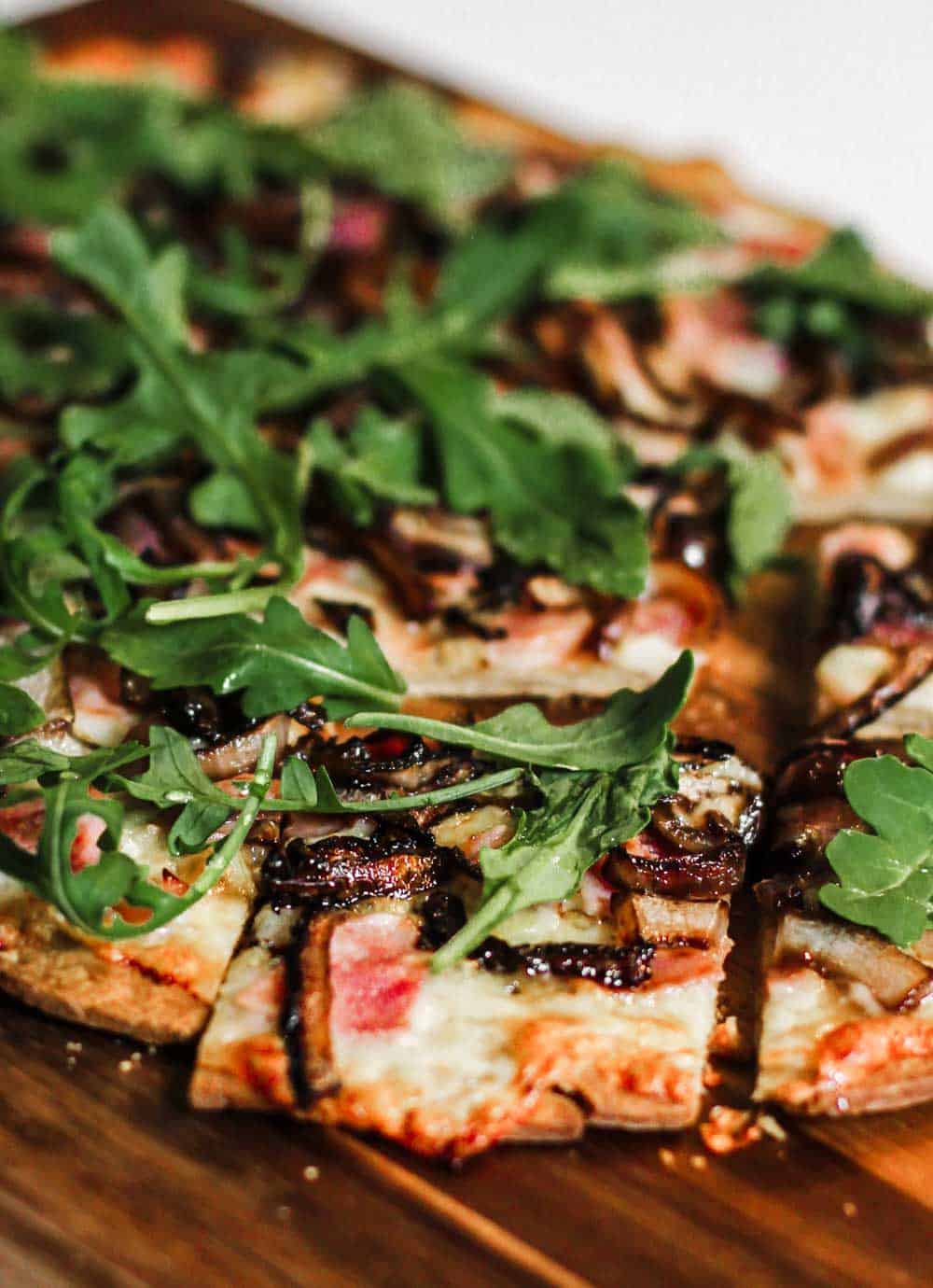 thin pizza with ham and arugula, sliced on wood board.