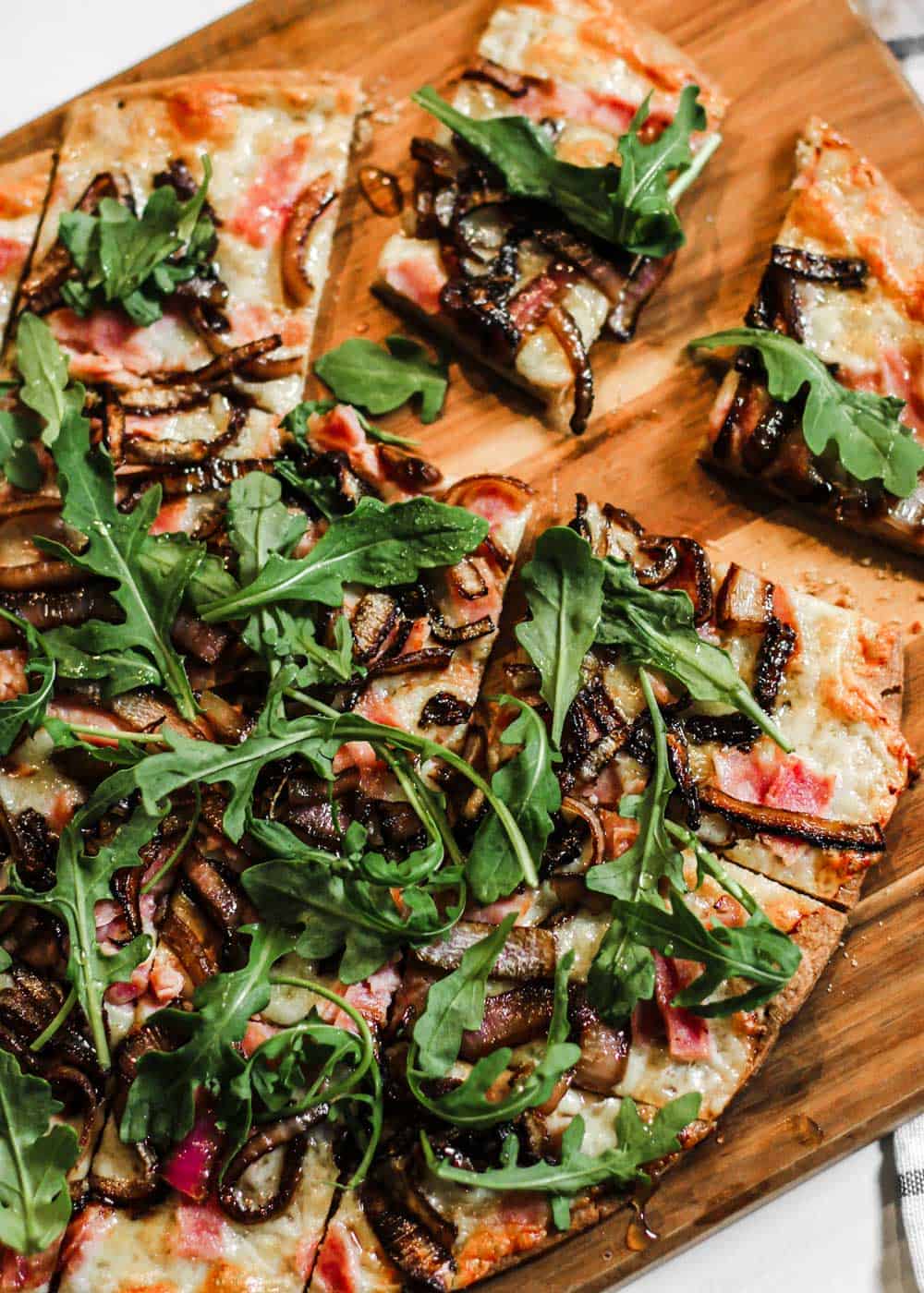 thin pizza with ham and arugula, on wood board.