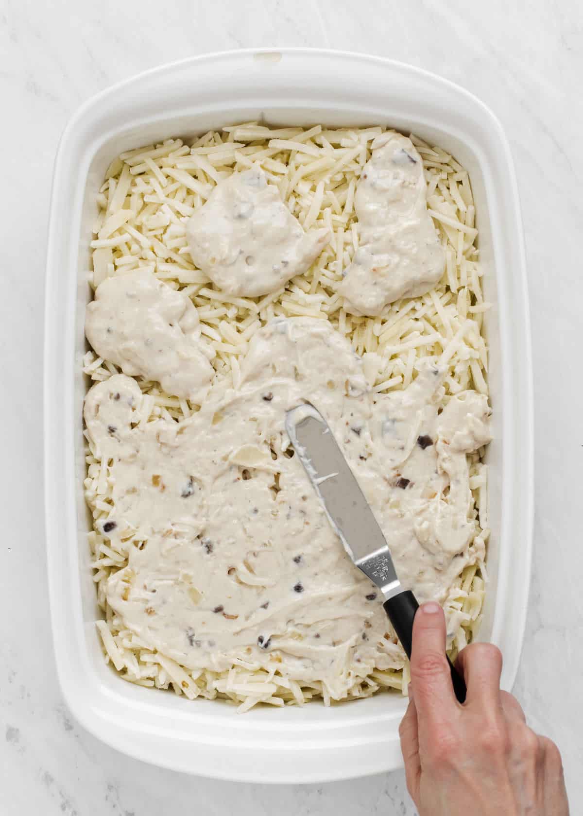 hash browns in white casserole dish with cream sauce being spread on top.