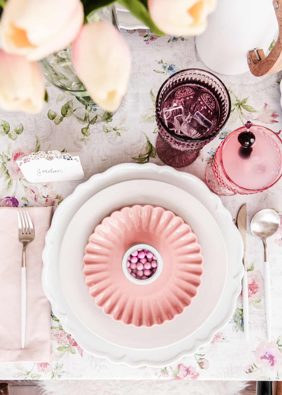 pink and white spring place setting with pink plate on top of white plate and charger and pink glasses and napkins, overhead.