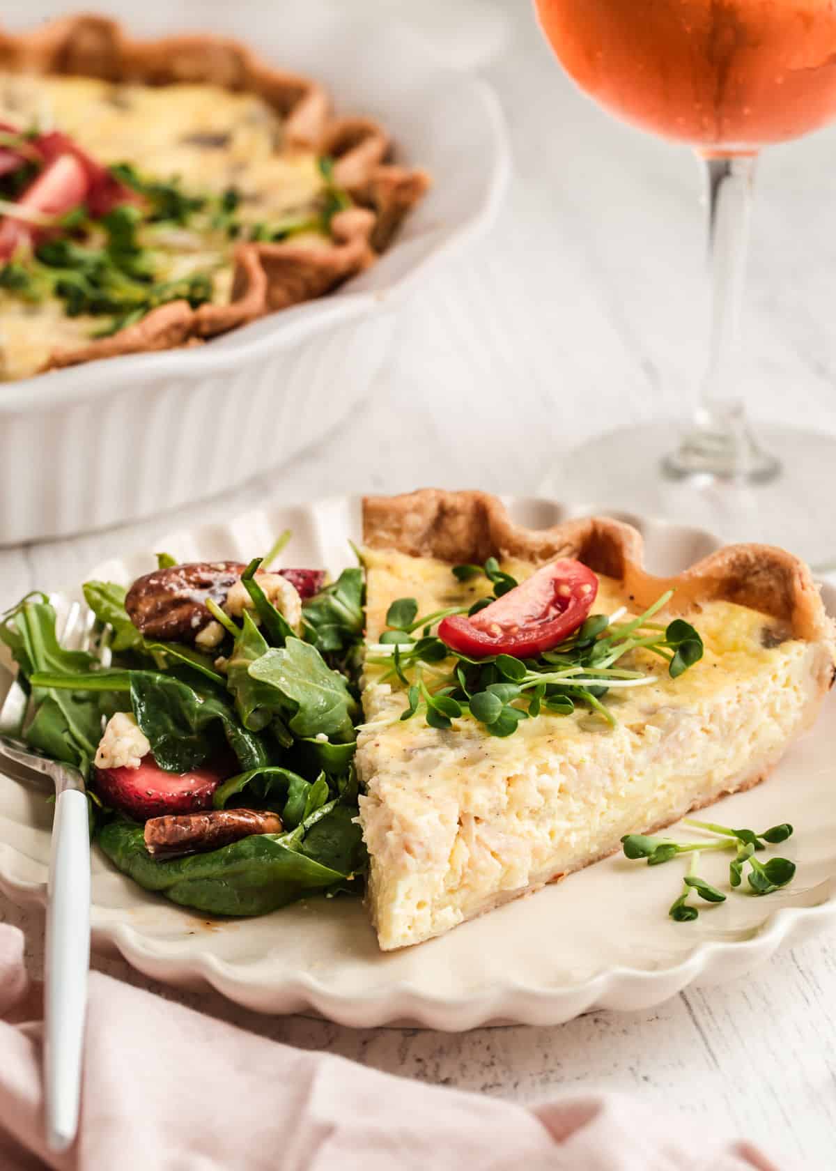 slice of quiche on white plate with salad on the side.