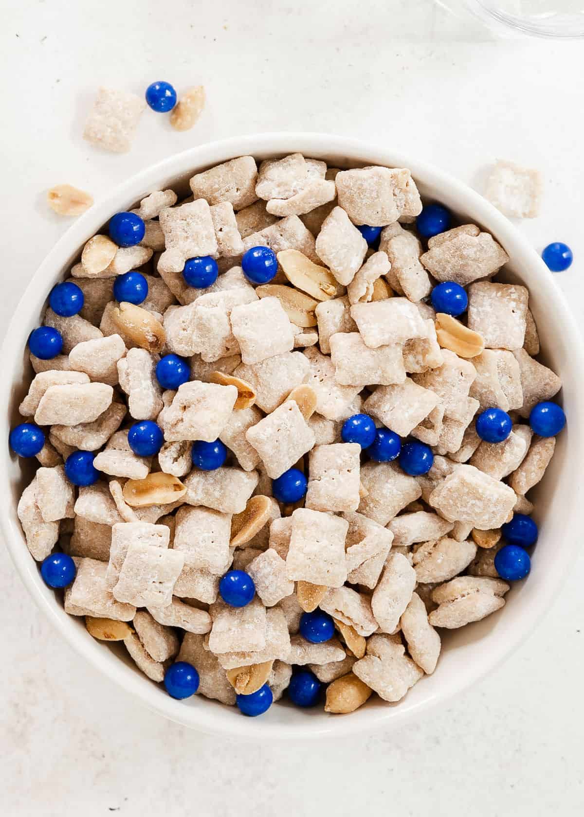 Chex muddy buddies with peanuts and blue candies in round bowl, overhead.
