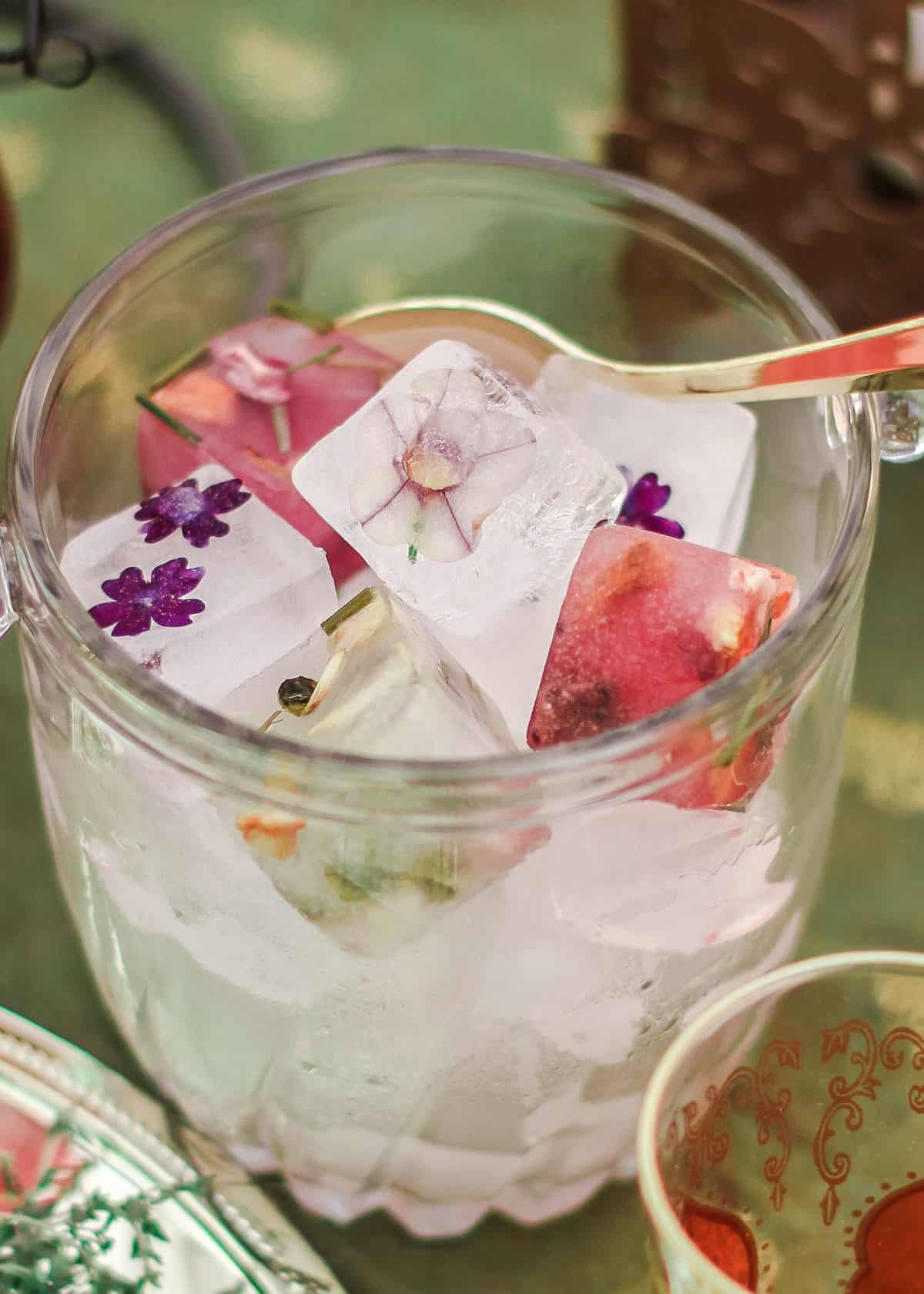 ice cubes with flowers frozen inside, in glass ice bucket.