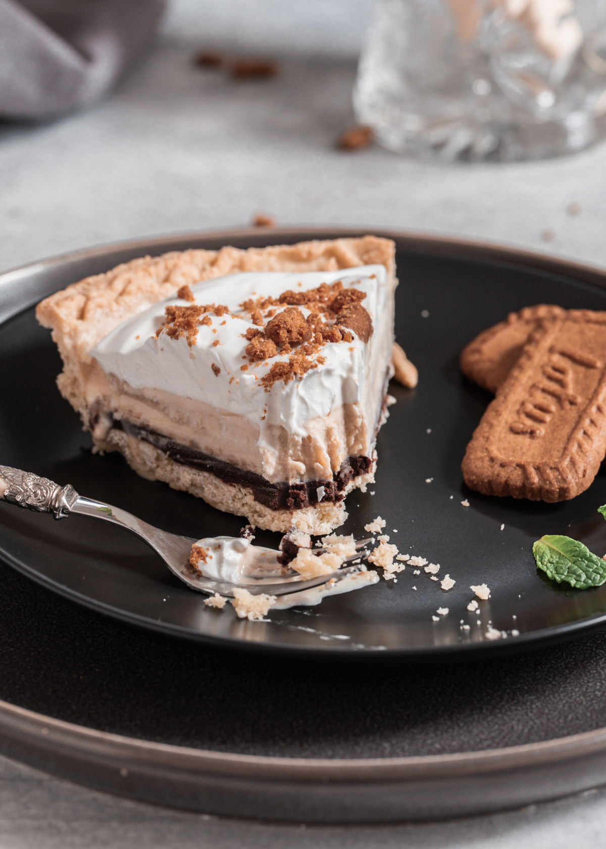 slice of ice cream pie with whipped cream on top and Biscoff cookies on the side, on black plate.